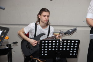 Ein junger Mann spielt eine Ibanez E-Gitarre neben einem Notenständer.